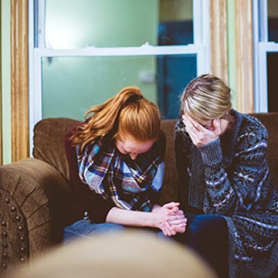 Two women sitting on a couch looking visibly upset